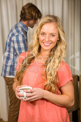 Blonde woman posing with a mug with her boyfriend behind