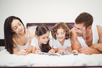 Children reading book with parents at home