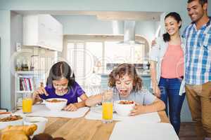 Children having breakfast while parents standing by table