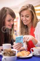 Two women looking at mobile phone while having snacks and coffee