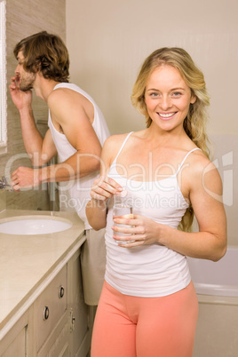 Blonde woman taking a pill with her boyfriend brushing his teeth