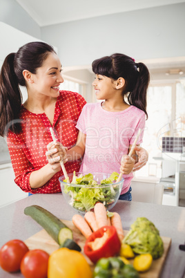 Happy mother and daughter preparing salad