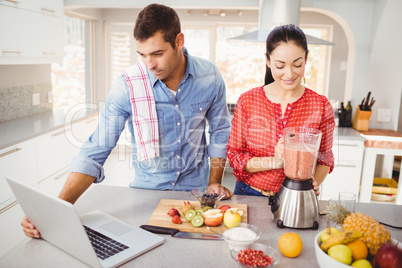 Couple standing with fruit juice while man using laptop