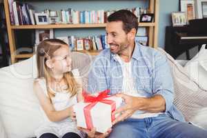 Smiling daughter giving gift to father while sitting on sofa