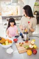 Smiling mother and daughter preparing fruit juice