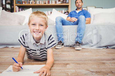 Portrait of boy drawing in book while father sitting on sofa
