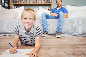 Portrait of boy drawing in book while father sitting on sofa