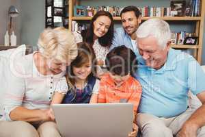 Smiling children and grandparents using laptop with family