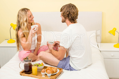 Cute couple having breakfast sitting on their bed