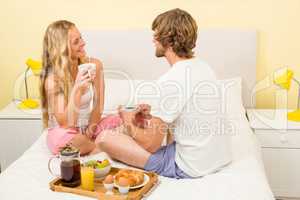 Cute couple having breakfast sitting on their bed