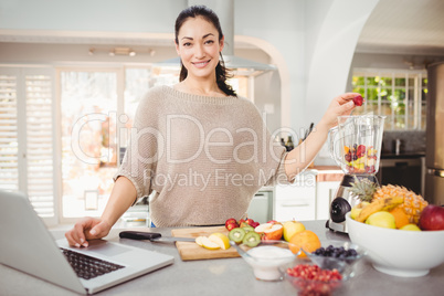 Portrait of smiling woman preparing fruit juice while working on