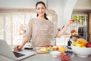 Portrait of smiling woman preparing fruit juice while working on