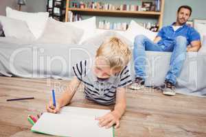 Boy drawing in book while father sitting on sofa