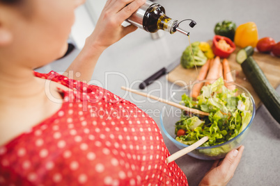 Midsection of woman adding oil in salad