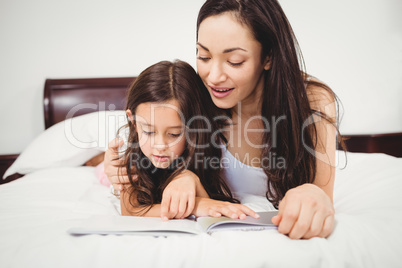 Daughter reading book with mother on bed