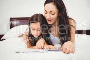 Daughter reading book with mother on bed