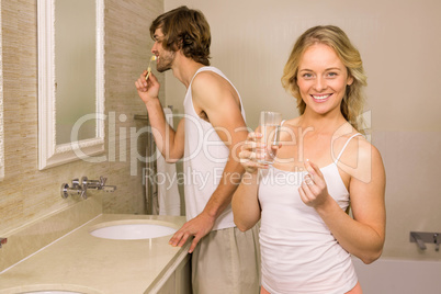 Blonde woman taking a pill with her boyfriend brushing his teeth
