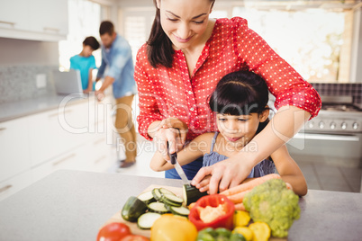Happy mother teaching daughter to cut vegetables