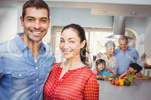 Portrait of happy couple with family preparing food in backgroun