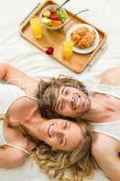 Cute couple lying in bed next to a breakfast tray