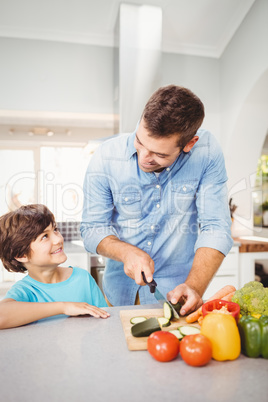 Man smiling while chopping vegetable with son