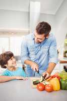 Man smiling while chopping vegetable with son