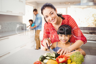 Portrait of happy mother teaching daughter to cut vegetables