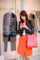 Beautiful woman using her phone while window shopping