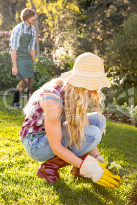 Gardener woman planting a flower with her boyfriend behind