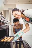 Happy woman with daughter placing cookies in oven