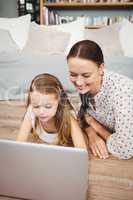 Happy daughter using laptop with mother while lying on hardwood