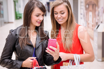 Two beautiful women looking at phone in shopping mall