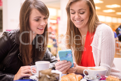 Two women looking at mobile phone while having snacks and coffee