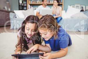 Siblings using digital tablet while parents in background