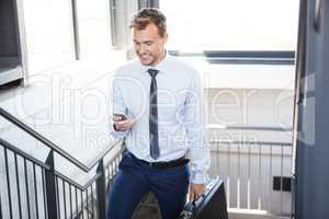 Businessman using phone and climbing staircase