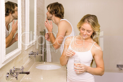 Blonde woman taking a pill with her boyfriend brushing his teeth