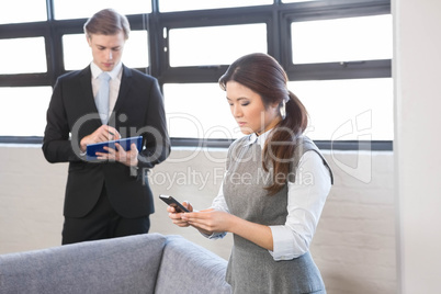 Businesswoman text messaging on smartphone and businessman using