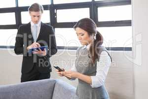 Businesswoman text messaging on smartphone and businessman using