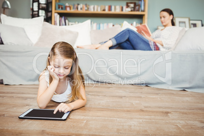Girl using digital tablet with mother reading book