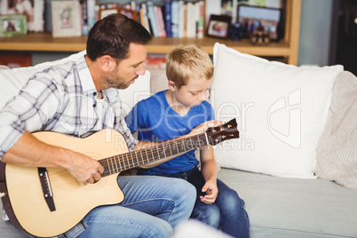 Father playing guitar with son sitting on sofa