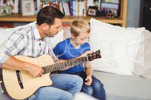 Father playing guitar with son sitting on sofa