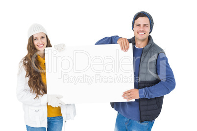 Happy couple in winter clothes holding a poster