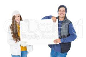 Happy couple in winter clothes holding a poster