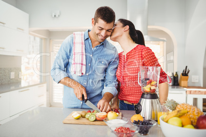 Woman kissing man preparing fruit juice