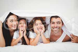 Happy family below blanket on bed at home