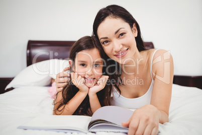 Portrait of mother and daughter with book on bed at home