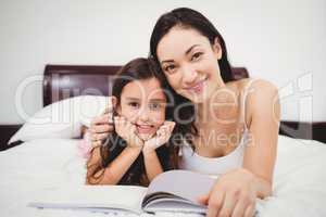 Portrait of mother and daughter with book on bed at home