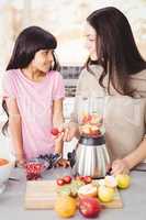 Cheerful mother and daughter preparing fruit juice