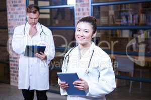 Female doctor standing near library with digital tablet