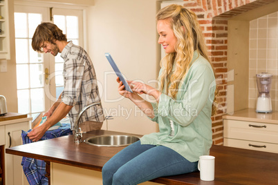 Pretty blonde using tablet while boyfriend ironing a shirt